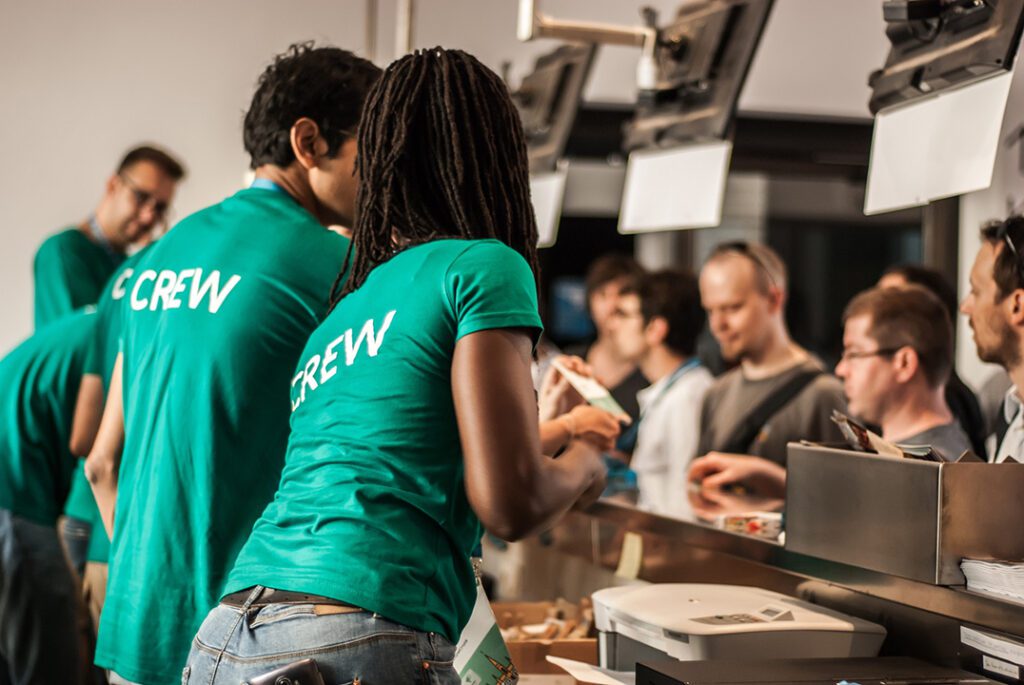 People in green t-shirts with the word 'crew' on the back serving people at a counter